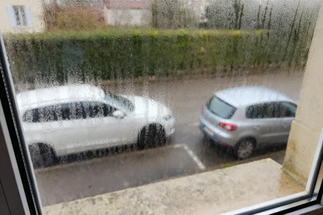 Voiture blanche et grise vues à travers la condensation fenêtre élevée.