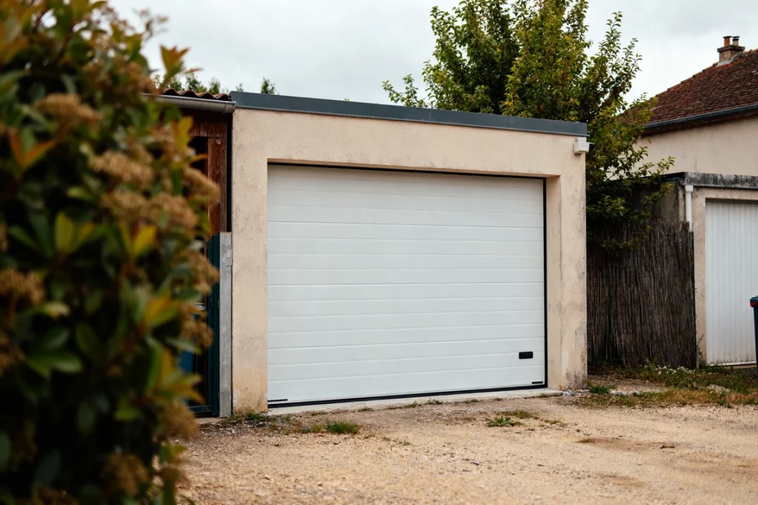 Porte de garage sectionnelle blanche fermée devant un garage en béton avec fabricant de porte