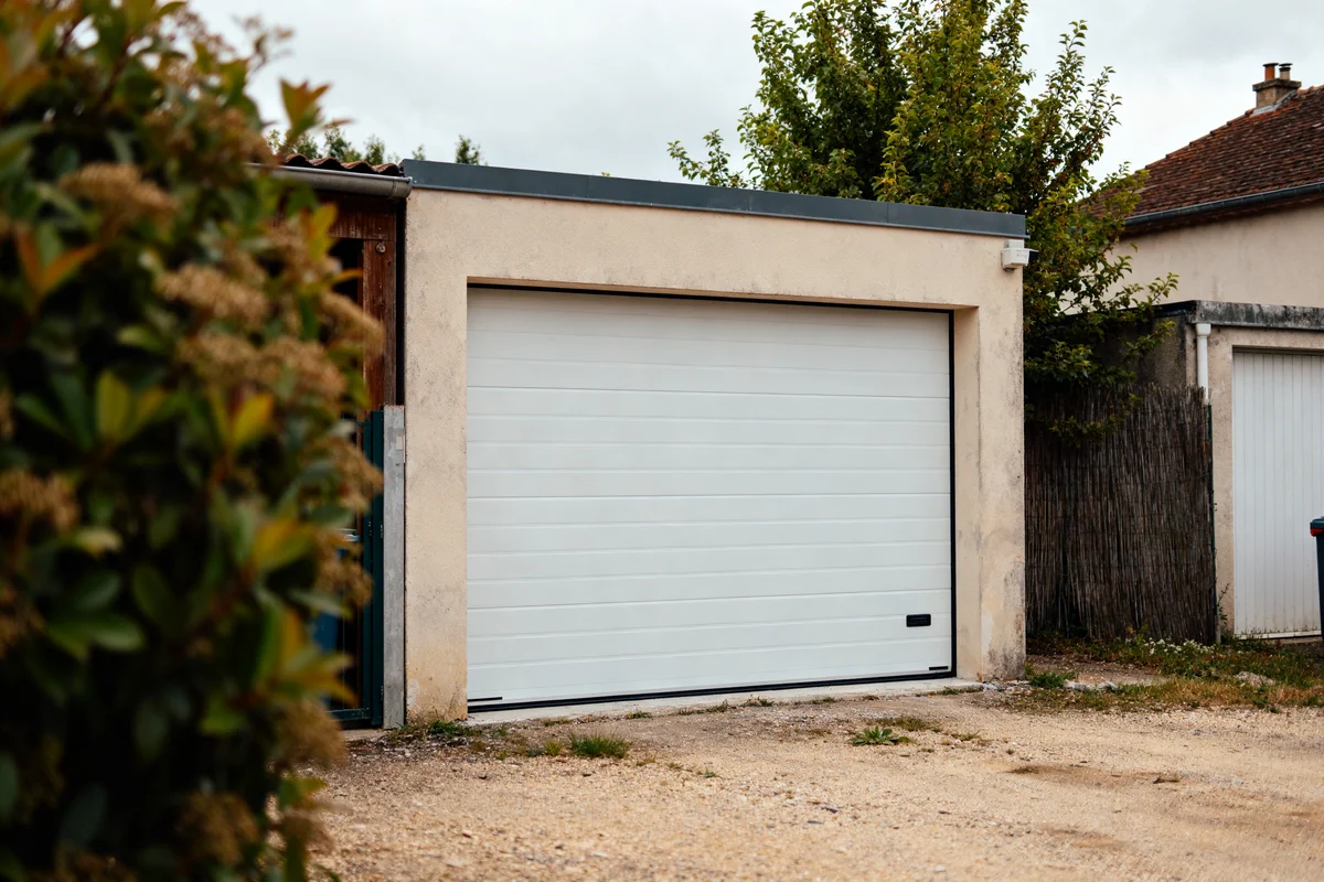 Porte de garage sectionnelle blanche fermée devant un garage en béton avec fabricant de porte
