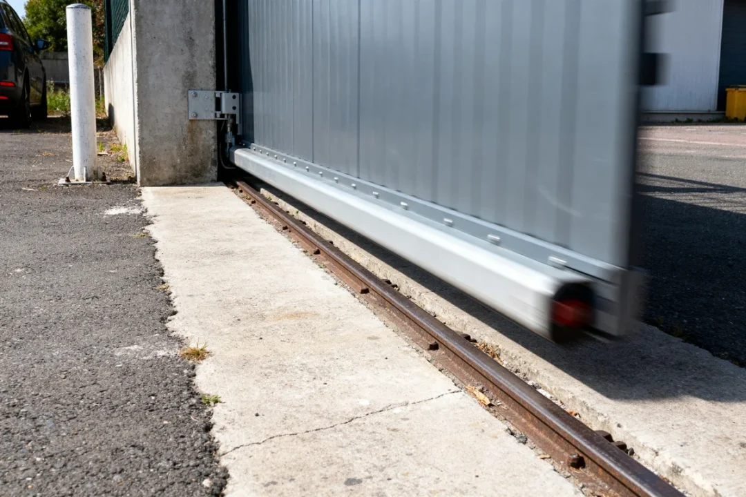 Portail coulissant gris en mouvement sur rails, guide pour portail coulissant.