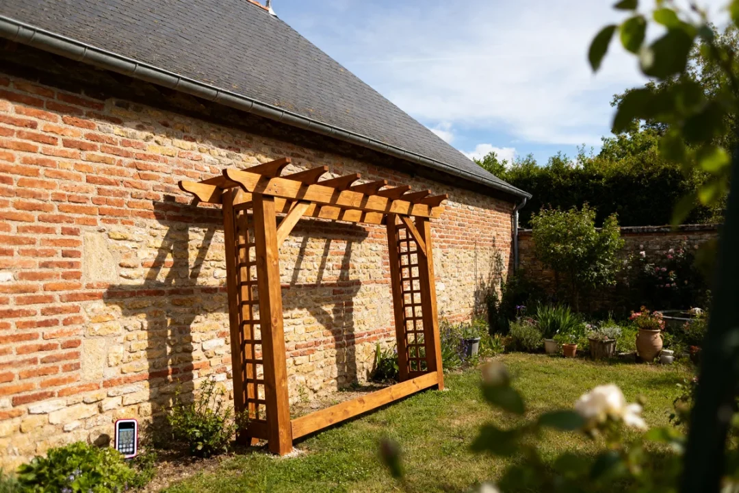 Maison en briques avec pergola adossée en bois dans un jardin ensoleillé
