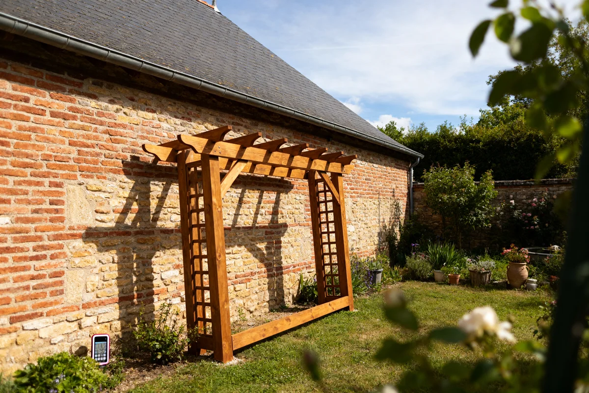 Maison en briques avec pergola adossée en bois dans un jardin ensoleillé
