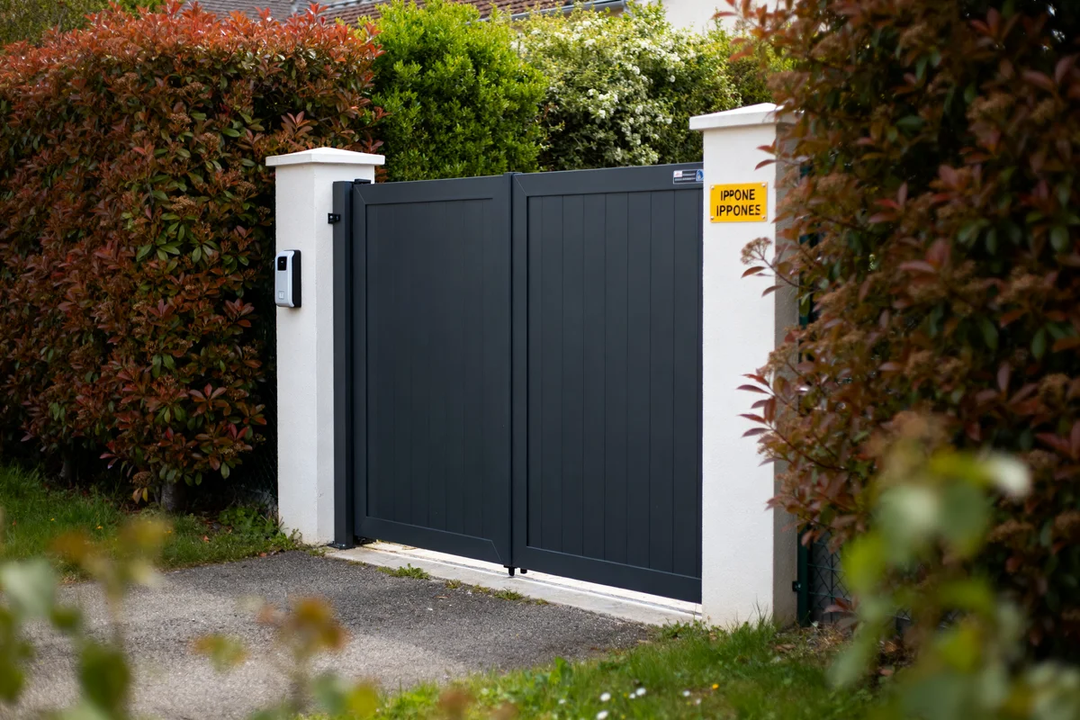 Portail électrique gris avec interphone entouré de haies prix abordable pour maison moderne