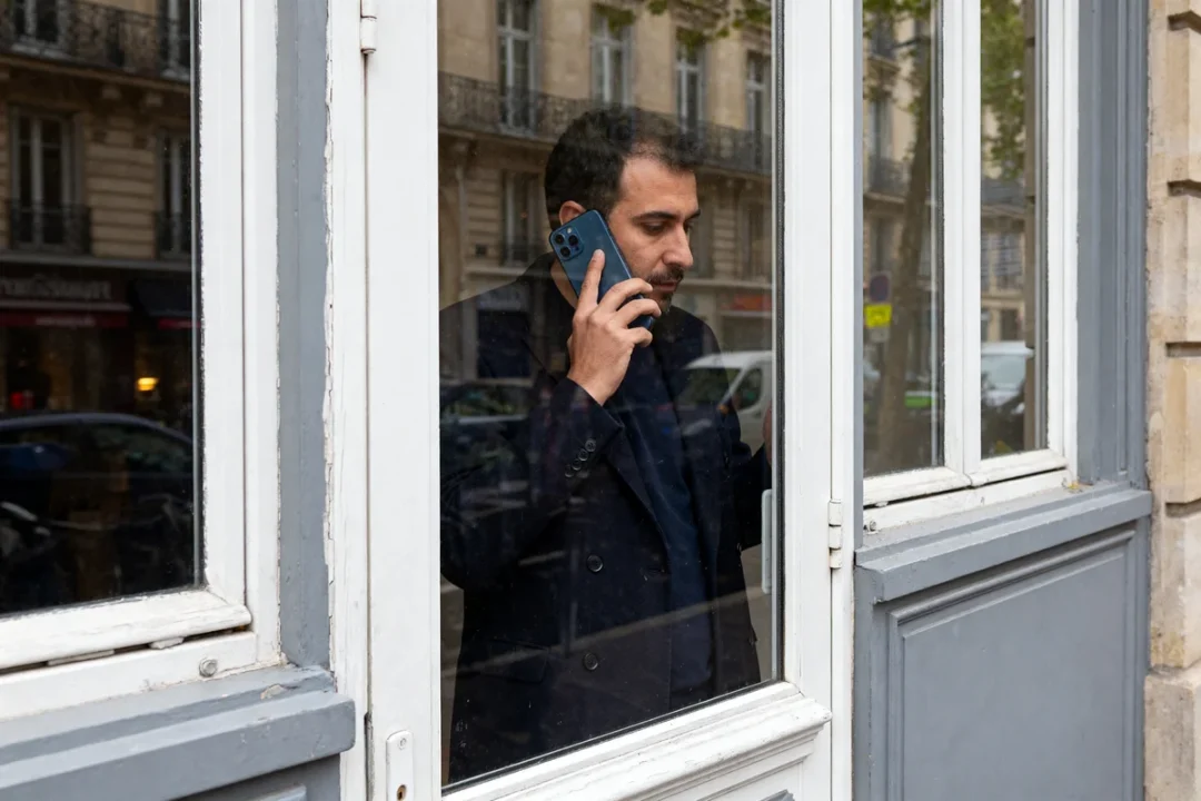 Homme au téléphone devant fenêtre PVC double vitrage vérifiant prix d'une fenêtre double vitrage pvc