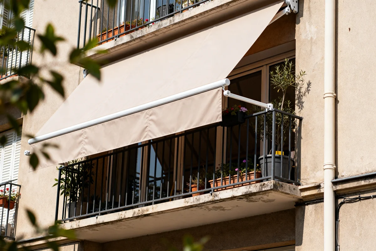 Balcon avec store banne sans percage beige, plantes en pots et rambarde métallique.